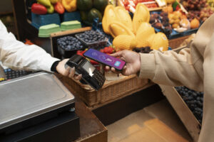 Pessoa utilizando o celular para fazer pagamento por aproximação em maquininha de cartão em supermercados.