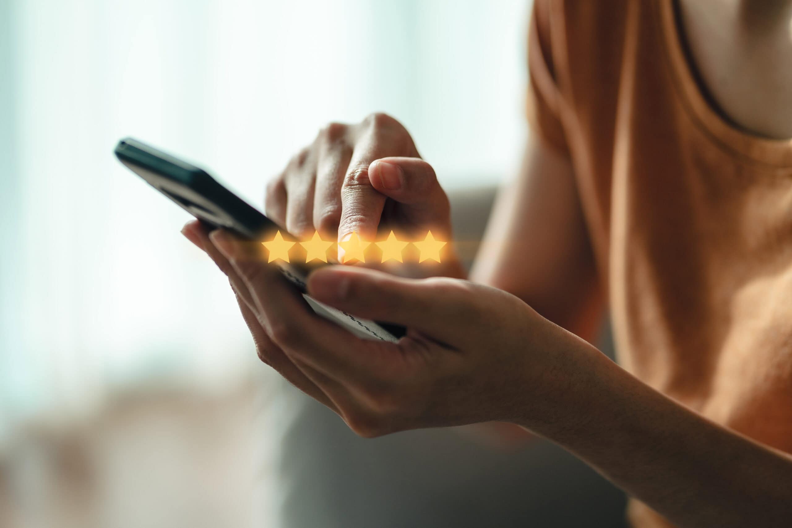 Pessoa utilizando um smartphone e tocando em uma avaliação de cinco estrelas, simbolizando uma experiência positiva de serviço.