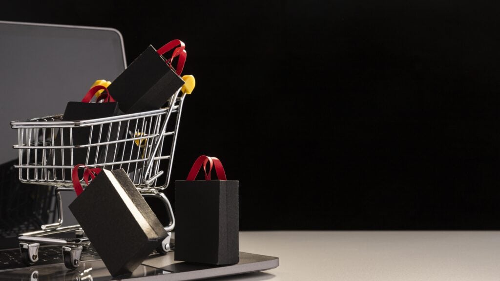Carrinho de compras com sacolas pretas sobre notebook, representando abandono de carrinho em lojas virtuais.