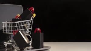Carrinho de compras com sacolas pretas sobre notebook, representando abandono de carrinho em lojas virtuais.