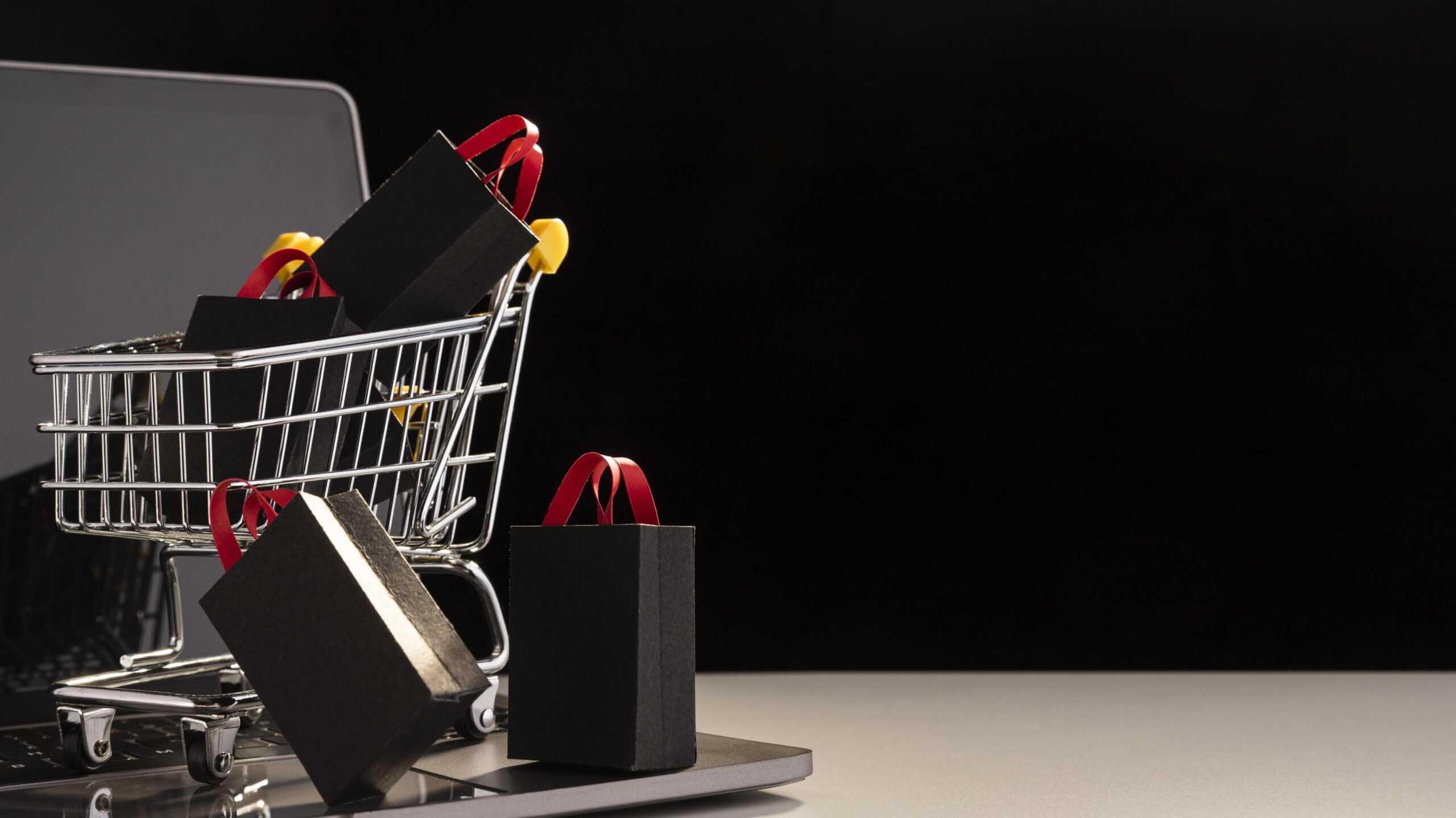 Carrinho de compras com sacolas pretas sobre notebook, representando abandono de carrinho em lojas virtuais.