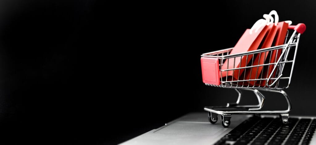 Mini carrinho de compras com sacolas vermelhas sobre notebook simbolizando abandono de carrinho no e-commerce.