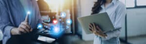 Duas pessoas usando tecnologia: à esquerda, alguém interage com um tablet, com ícones digitais de redes sociais e comunicação flutuando; à direita, uma pessoa segura um laptop.