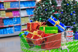 Carrinho de supermercado cheio de presentes coloridos, com decoração de Natal e prateleiras ao fundo.