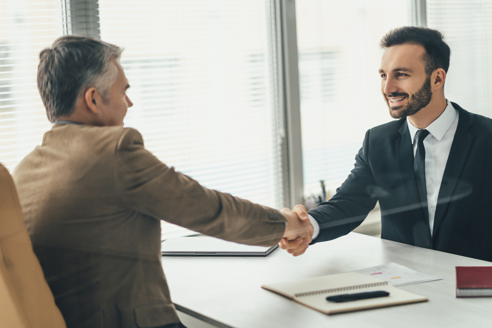 Dois executivos apertando as mãos em escritório, selando acordo em ambiente corporativo.