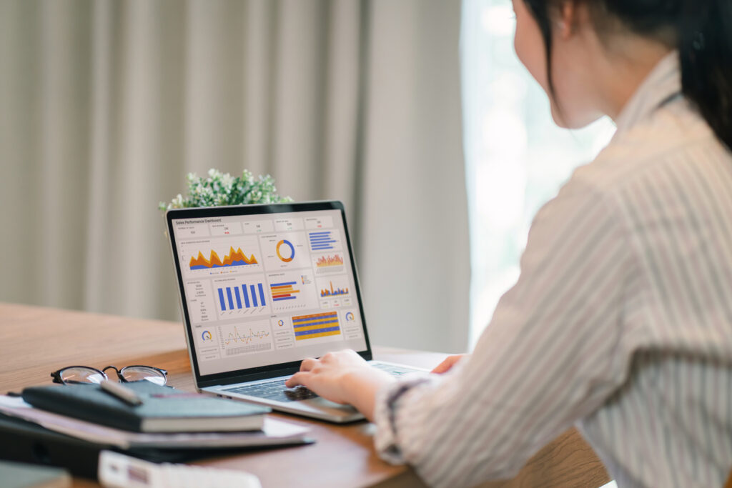 Pessoa trabalhando em um notebook sobre a mesa, analisando gráficos e indicadores de desempenho exibidos na tela.