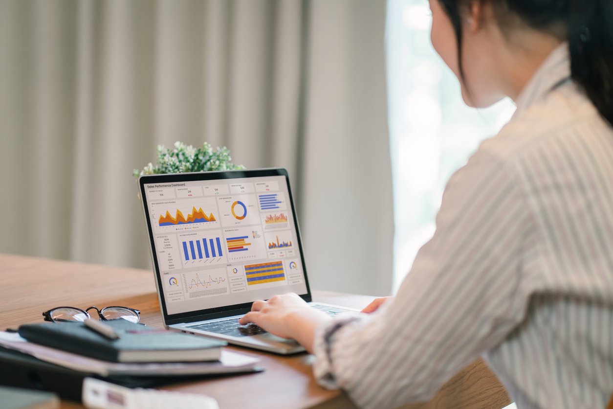 Pessoa trabalhando em um notebook sobre a mesa, analisando gráficos e indicadores de desempenho exibidos na tela.