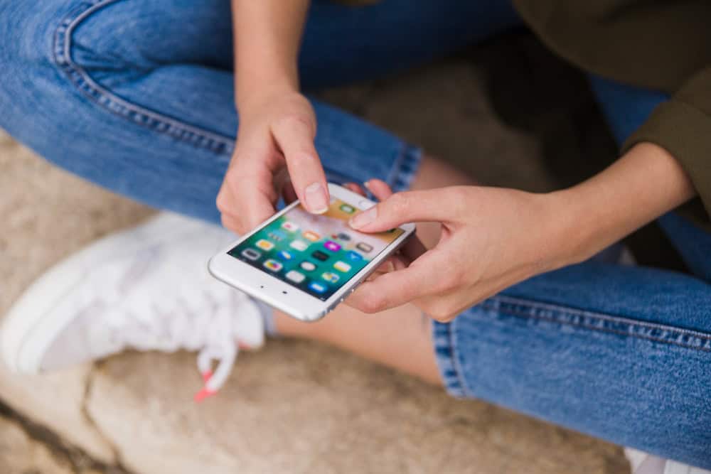 Pessoa sentada usando smartphone com aplicativos abertos na tela, segurando o aparelho com as duas mãos.
