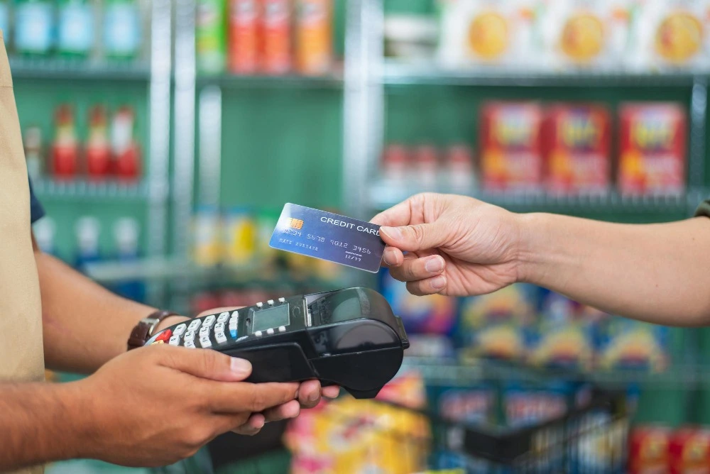 Pessoa realiza pagamento com cartão de crédito em uma máquina de cartão em um supermercado.